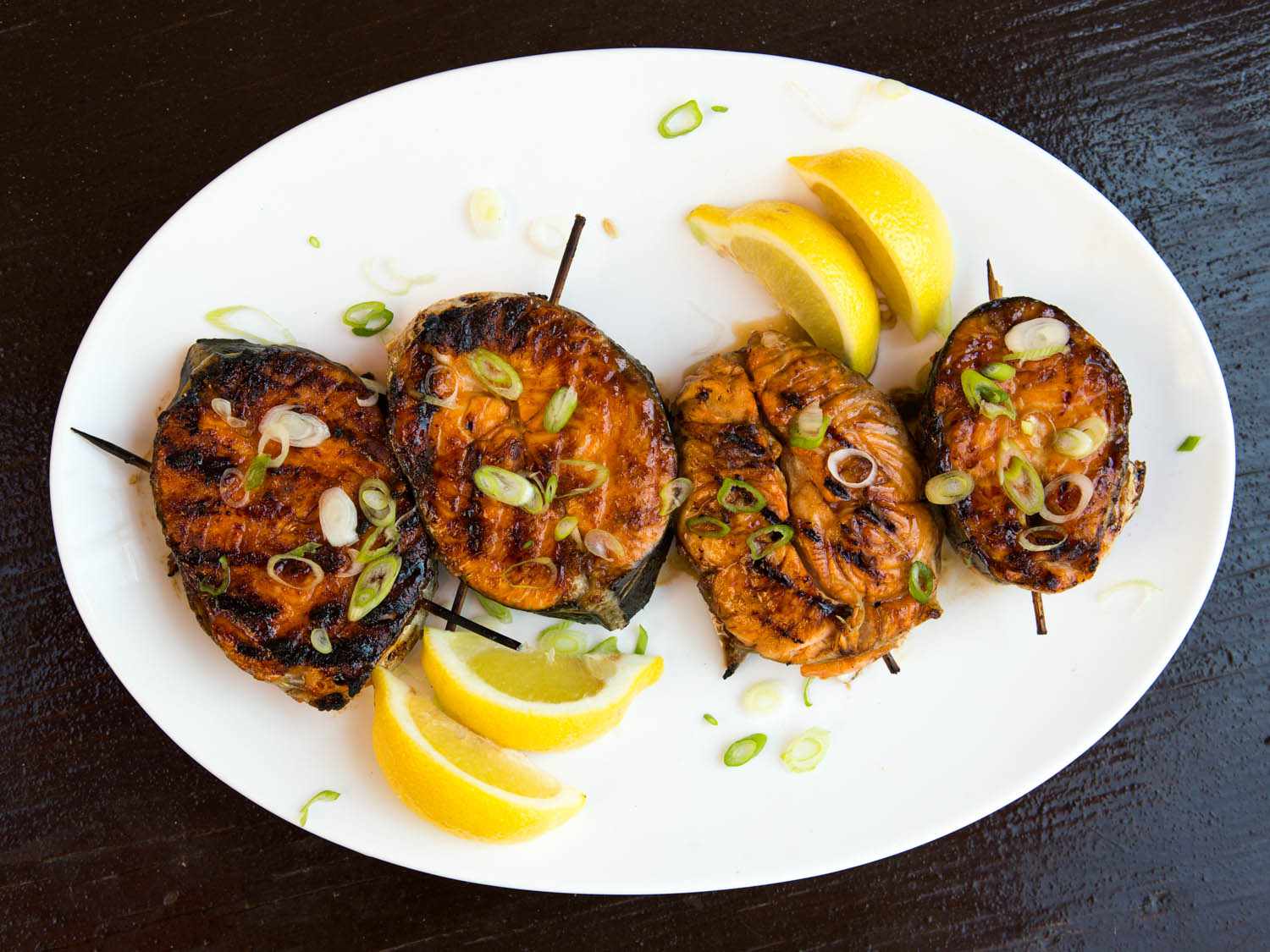 A platter of finished grilled salmon steaks with sliced scallions and lemon wedges.