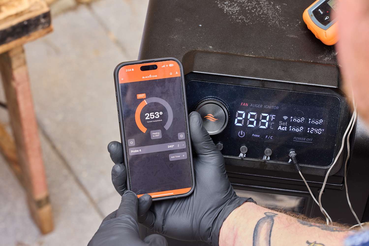 A person adjusts the temperature of the Blackstone 900 Pellet Grill on their smartphone