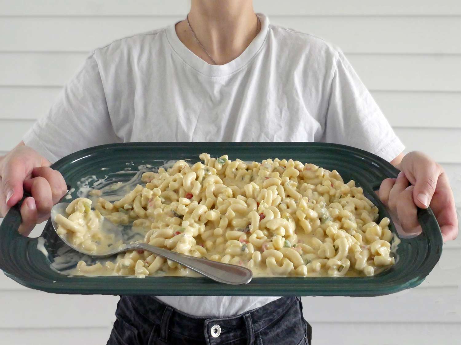 a person holding the le creuset platter with macaroni salad in it