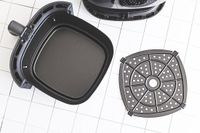 An open air fryer basket with its detachable tray displayed on a tiled surface
