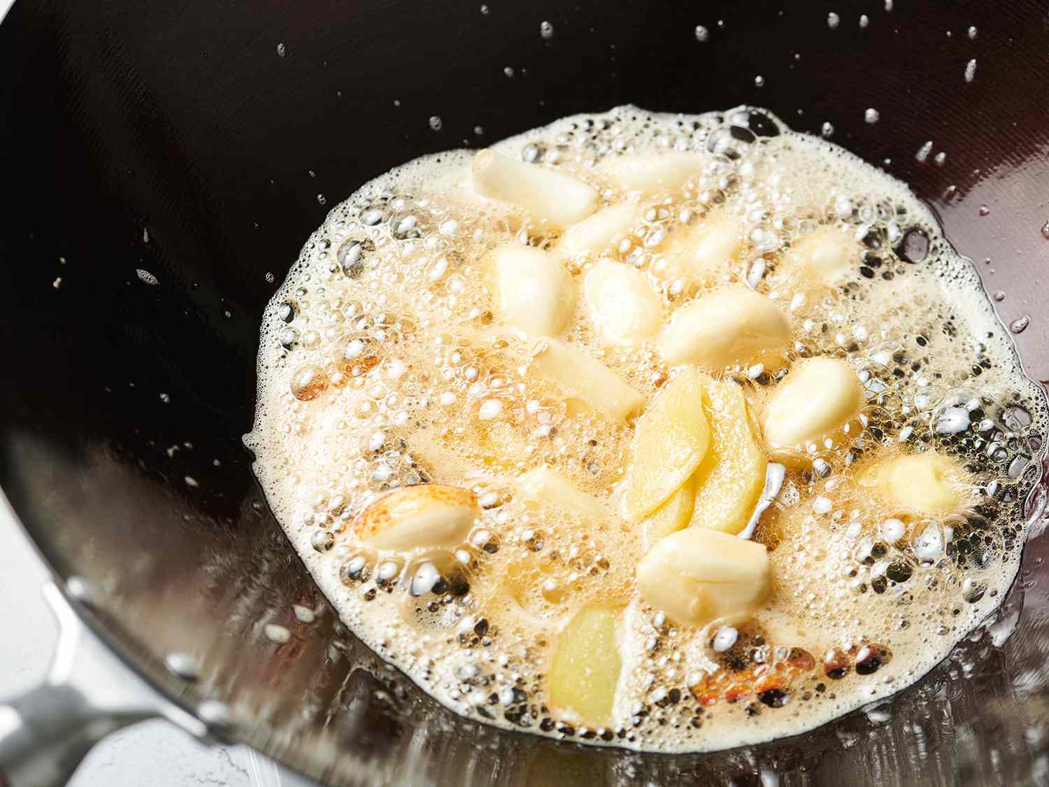 Garlic being fried in foaming oil inside of a wok.
