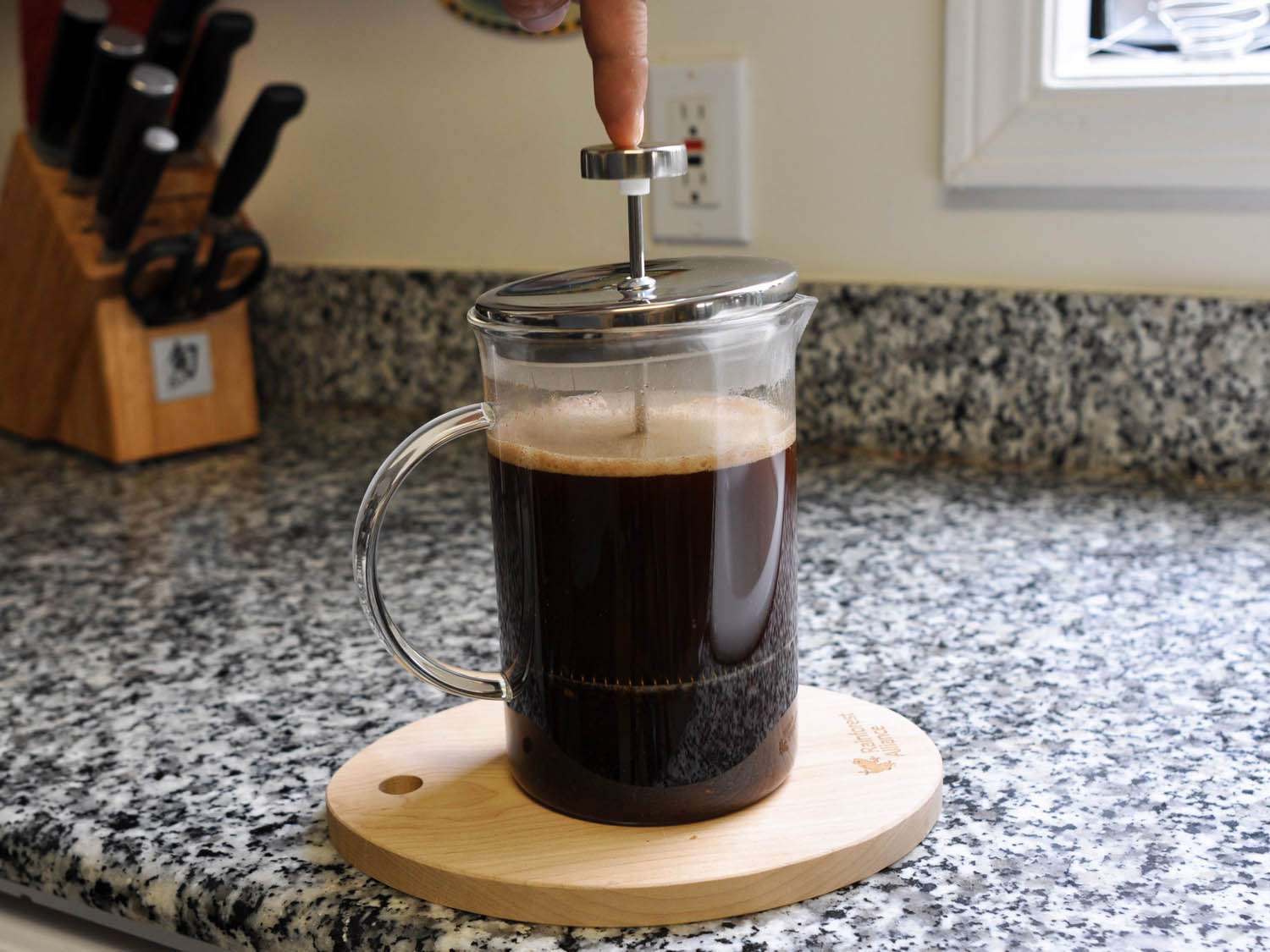The plunger of a glass French press being pressed down to brew coffee.