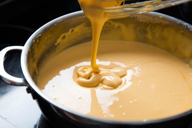 Thick cheese sauce dribbling off of a whisk into a saucepan full of more cheese sauce.