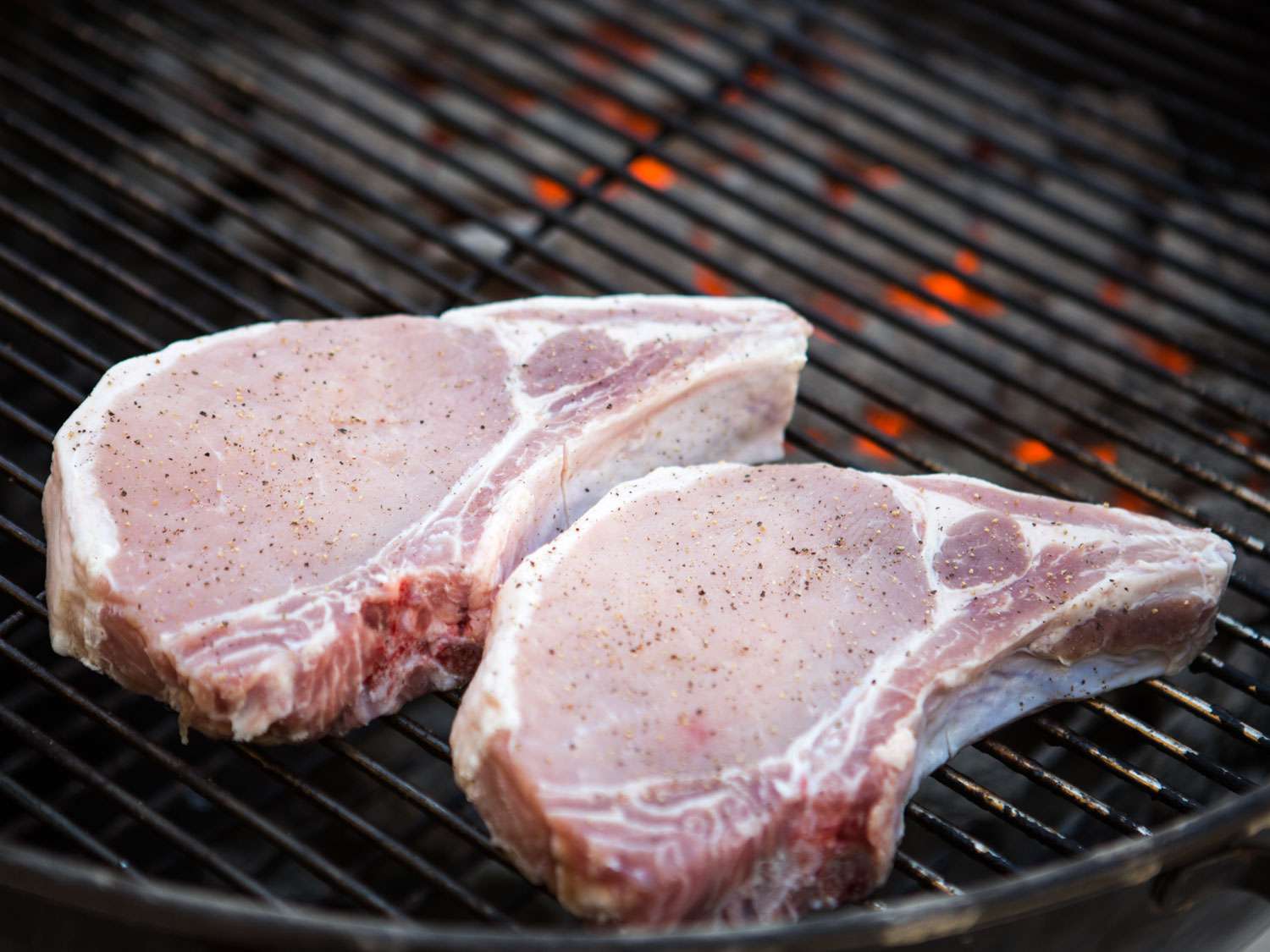Raw, seasoned pork chops placed on a charcoal grill for cooking.