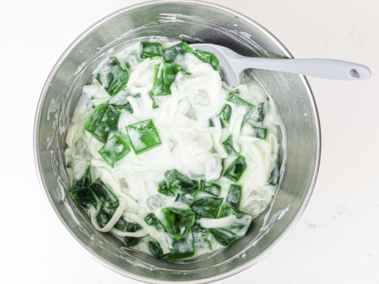 Coconut cream, condensed coconut milk, nata de coco, macapuno, and jelly squares mixed together in a metal bowl