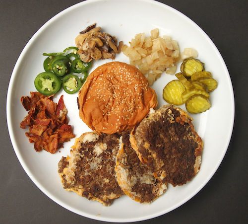 Overhead view of the components of a cheese burger from Five Guys, disassembled and laid out on a white platter.