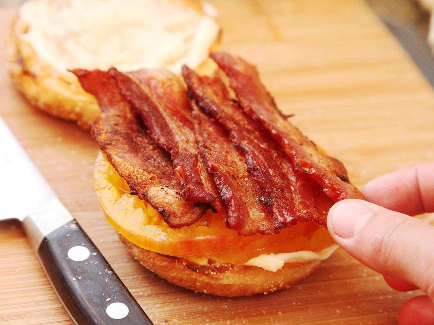 Laying bacon strips on top of tomato and mayo on a toasted English muffin half