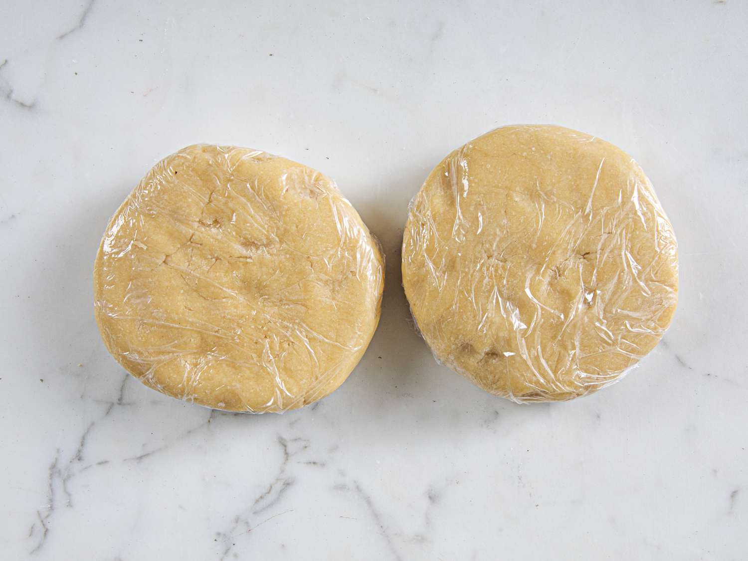 Two discs of dough wrapped in plastic wrap on a counter