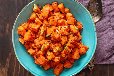 A bowl of roasted sweet potatoes with scallions.