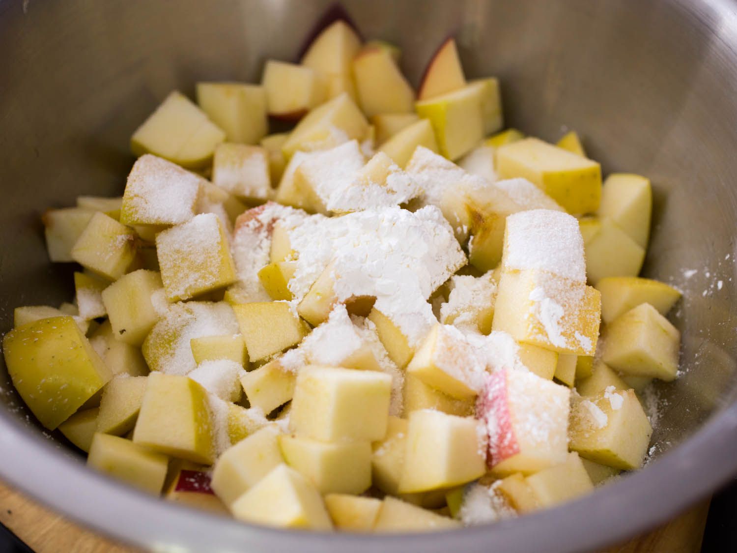 Chopped apple in a metal bowl with cornstarch and sugar sprinkled on top.
