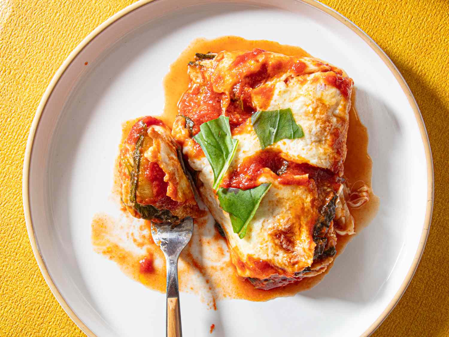 A plate with a zucchini parmesan dish garnished with basil accompanied by a fork