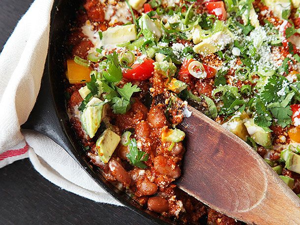 A wooden spoon in a cast iron pan of homemade chorizo and pinto bean chili.