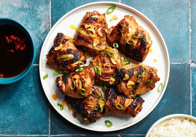 Chicken Inasal on a white plate next to dipping sauce and a bowl of white rice.