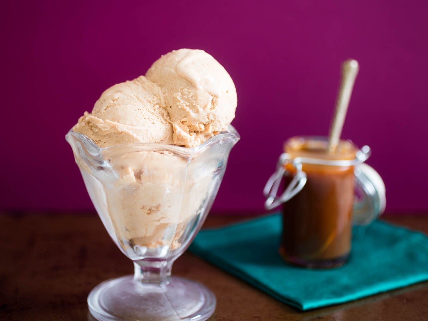 A parfait glass holding three scoops of cajeta ice cream with a small jar of cajeta in the background.