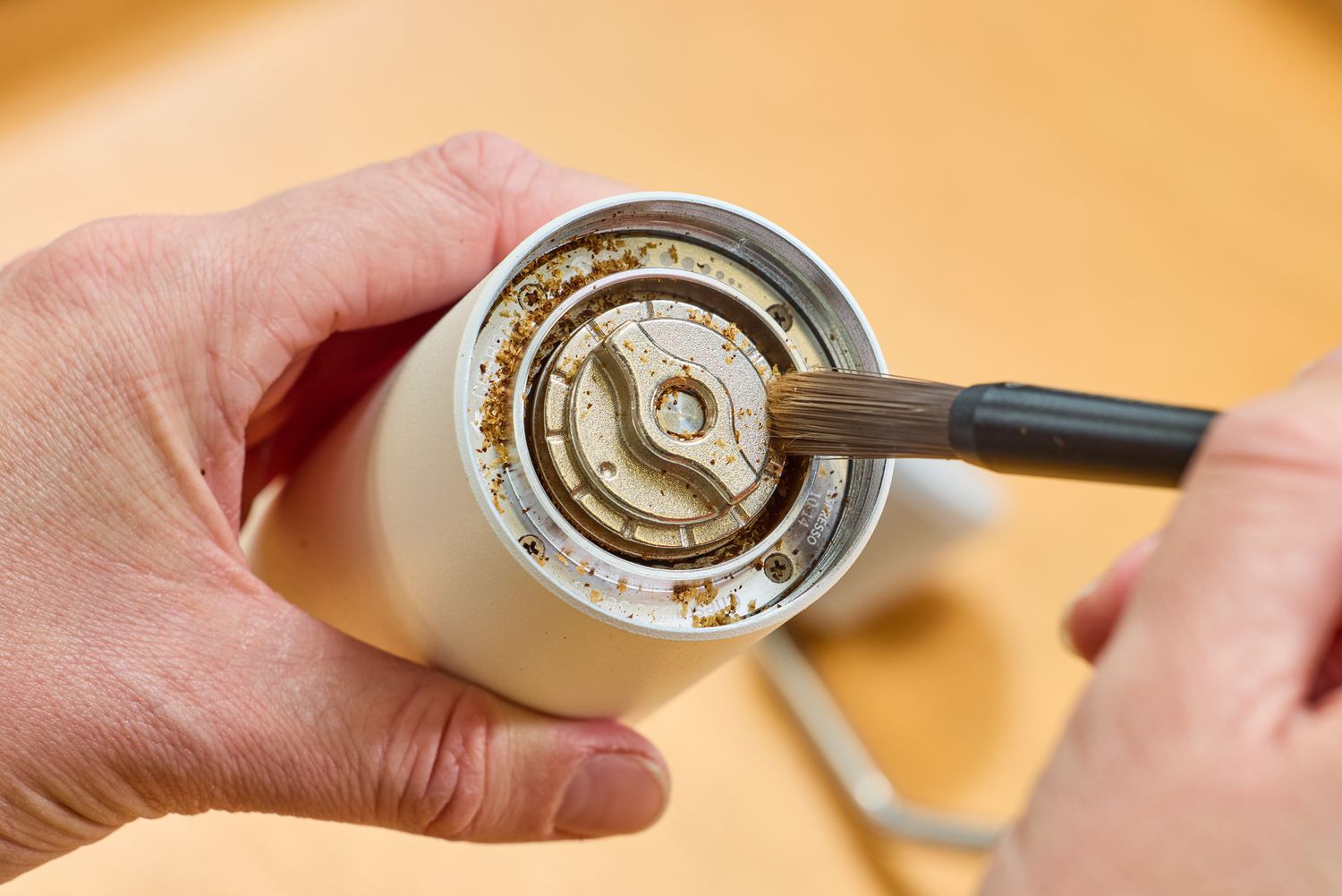 A person uses a brush to clean the Timemore C2 Max Manual Grinder