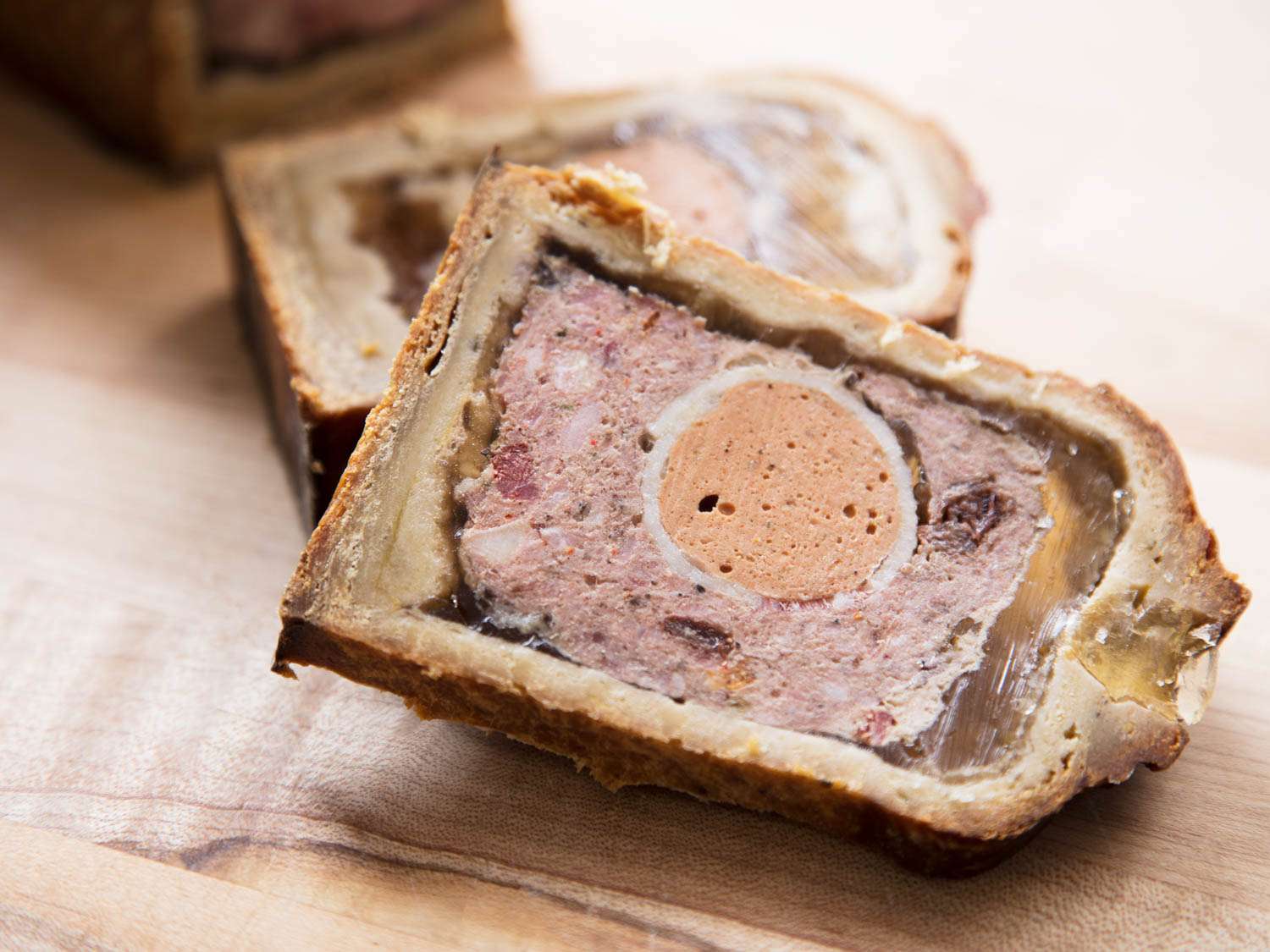 A slice of pâté en croûte. The pâté is set in gelée and is studded with interior garnishes, including whole hard-boiled eggs.