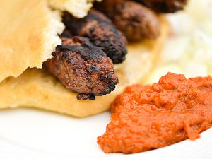 Close-up of cevapi tucked inside Serbian bread with roasted red pepper and eggplant sauce on the side