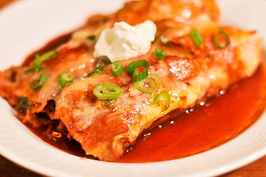 A plate with two red sauce enchiladas garnished with sour cream.