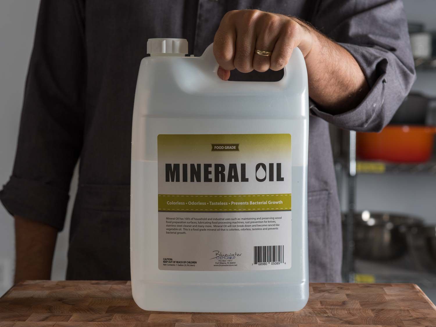 Hand holding a large jug of mineral oil on a wooden counter.