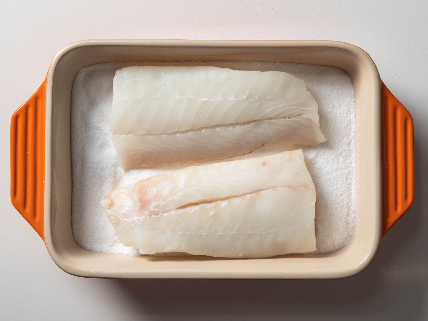 Cod fillets getting packed in salt in in a baking dish 