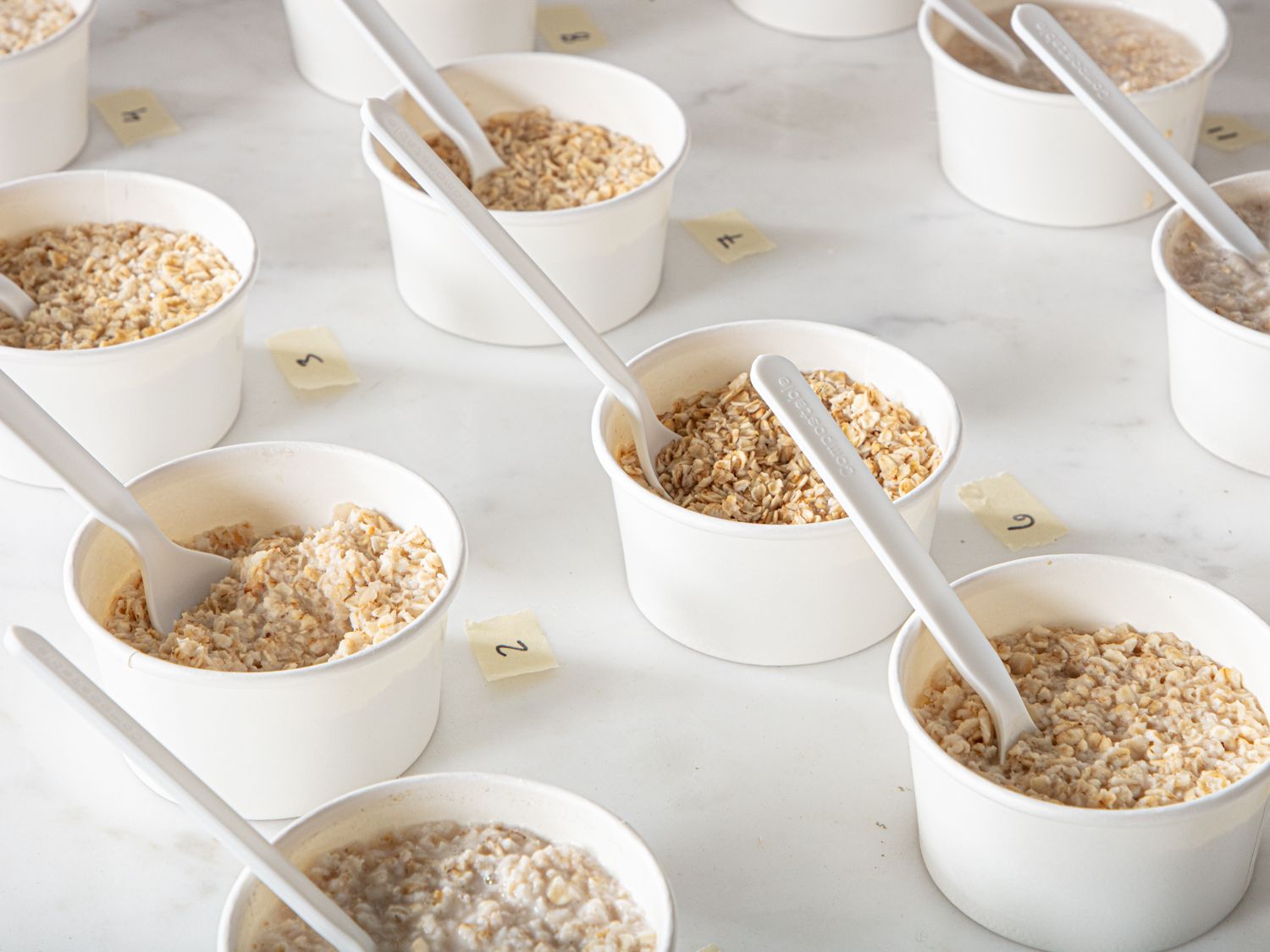 Multiple small cups each containing oatmeal arranged on a surface with plastic spoons and small numbered labels