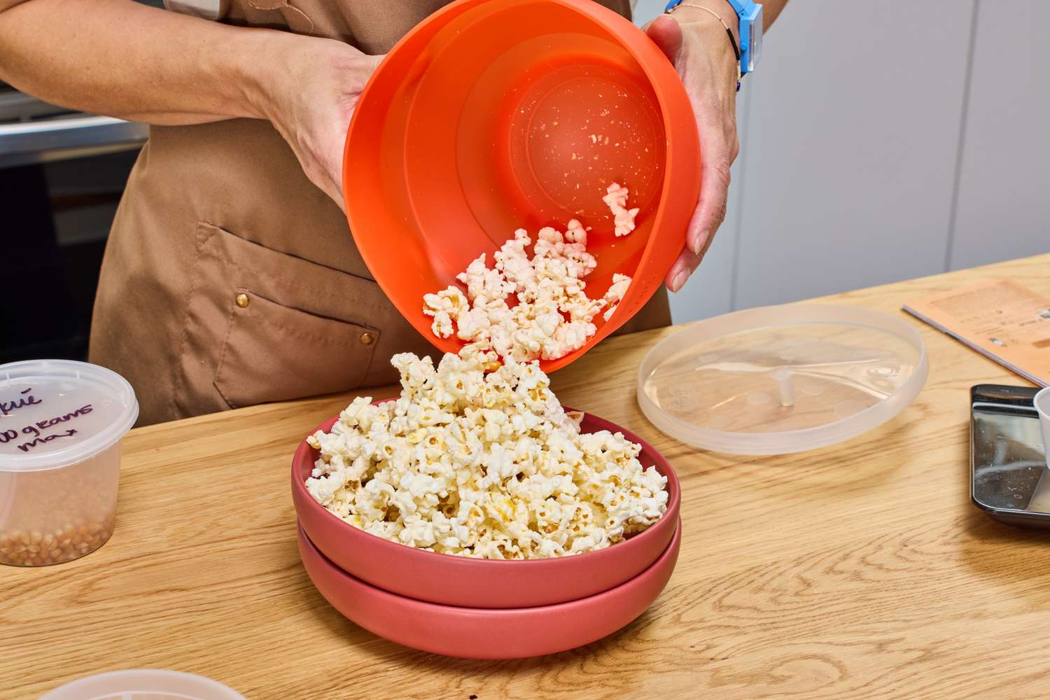 A person pours popcorn popped in the Lékué Popcorn Maker into a bowl