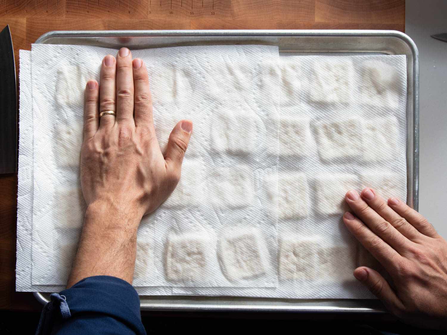 Hands pressing paper towel down over squares of tofu on baking sheet.