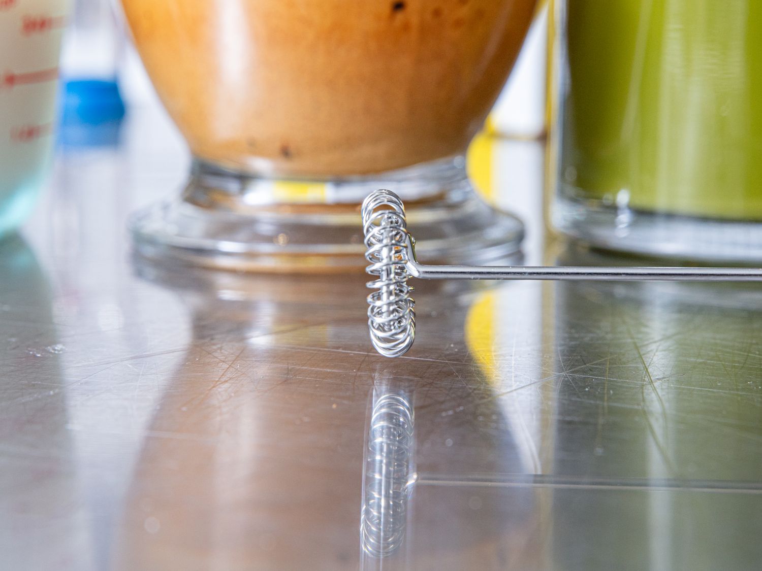 Closeup of a milk frother placed on a reflective surface with drinks in the background