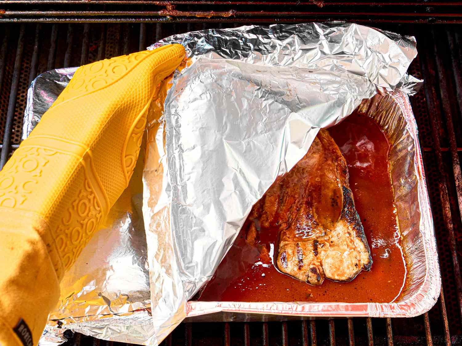 Grilled pork steak being uncovered from foil on a barbecue grill