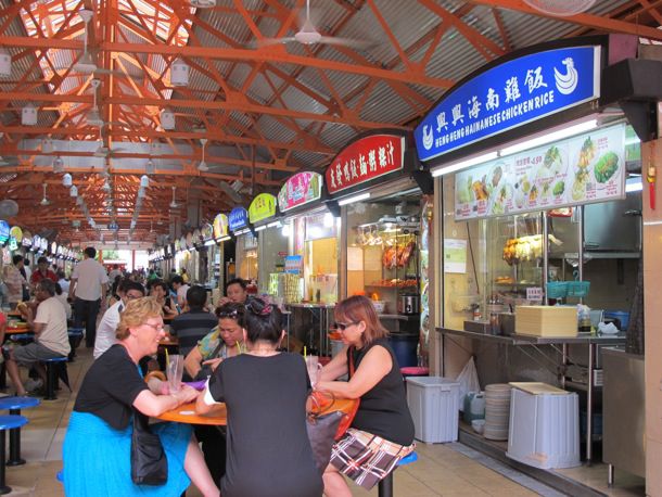 Singapore's Maxwell Food Centre, an open-air market bustling with diners. Small food stalls line the walls.