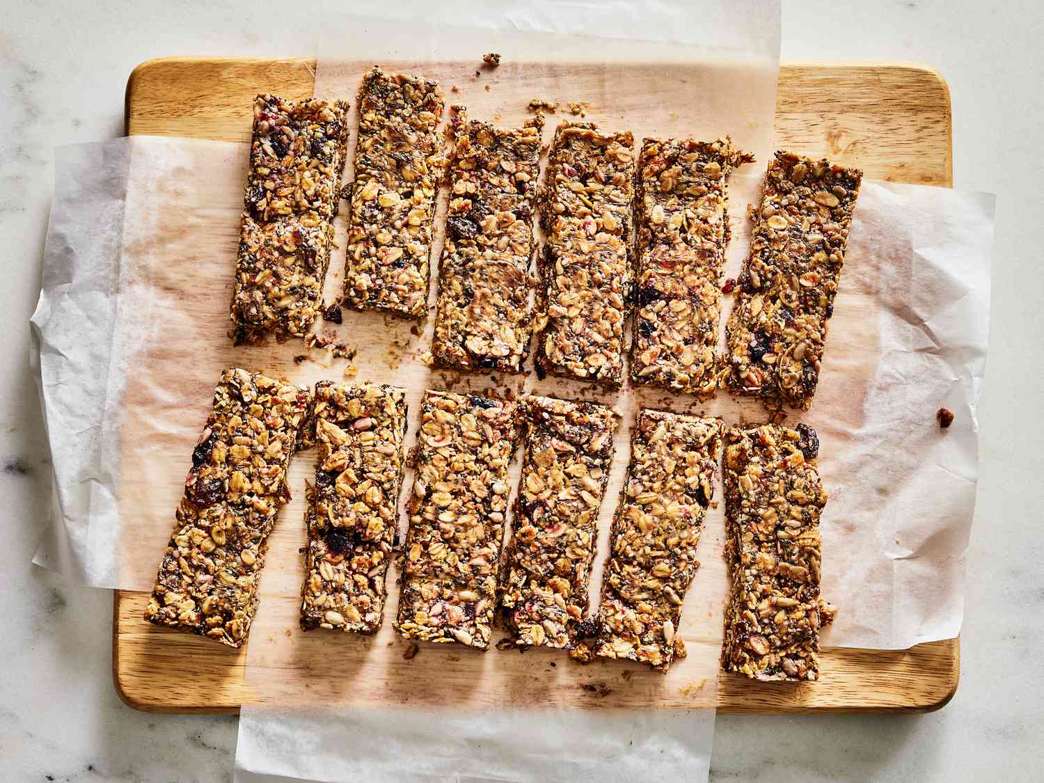 Granola bars cute into rectangles on parchment paper on top of a cutting board.