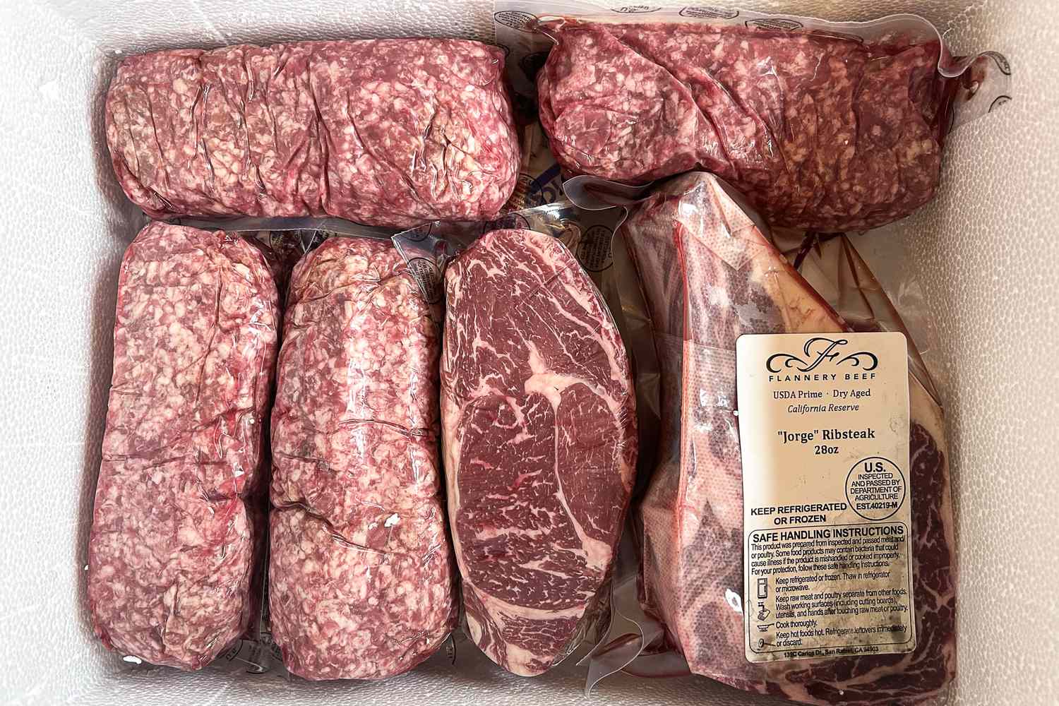 Vacuum sealed cuts of beef including ribeye and ground beef arranged in a foam container for delivery