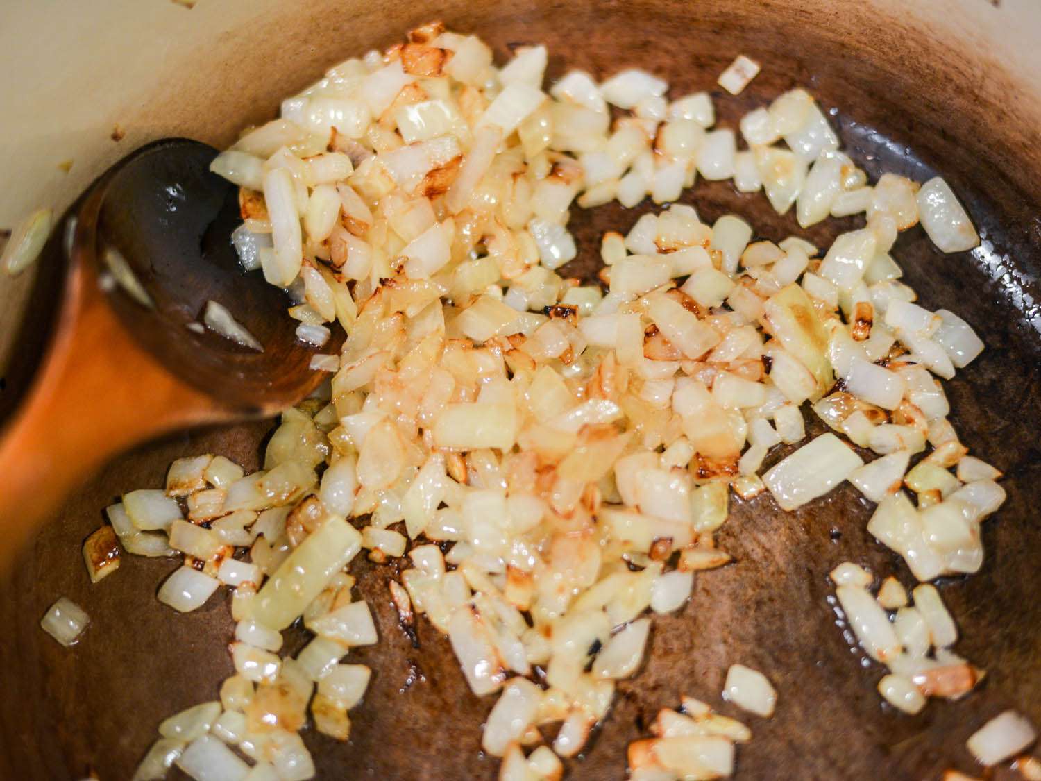 Wooden spoon stirring chopped onions browning inside a pot