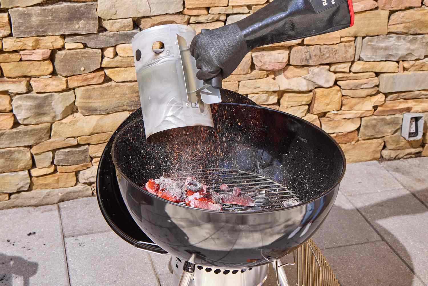 A hand adding hot coals to the Weber Original Kettle Premium 22-Inch Charcoal Grill