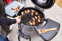 A person cooks chicken in the Broil King Keg Kamado Charcoal Grill