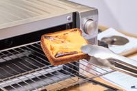 Tongs lifting cheese toast from the Breville the Mini Smart Oven BOV450XL