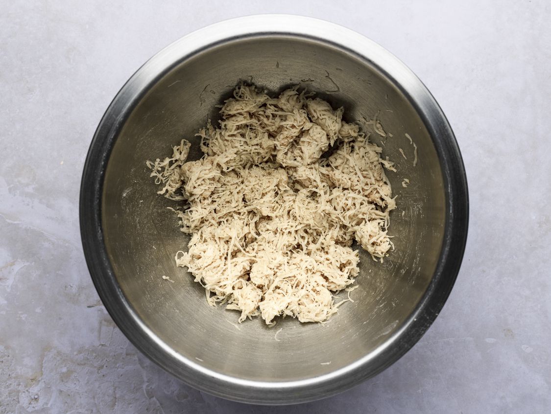 Drained shredded potato mixed with salt and pepper in a metal bowl.