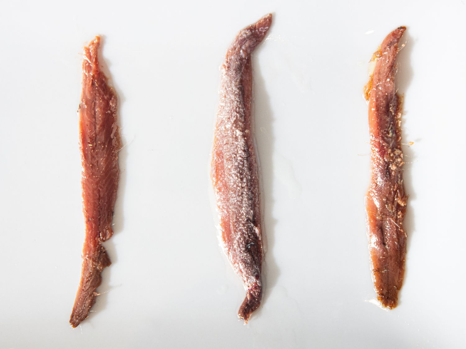 Three anchovy filets laid out on a white surface