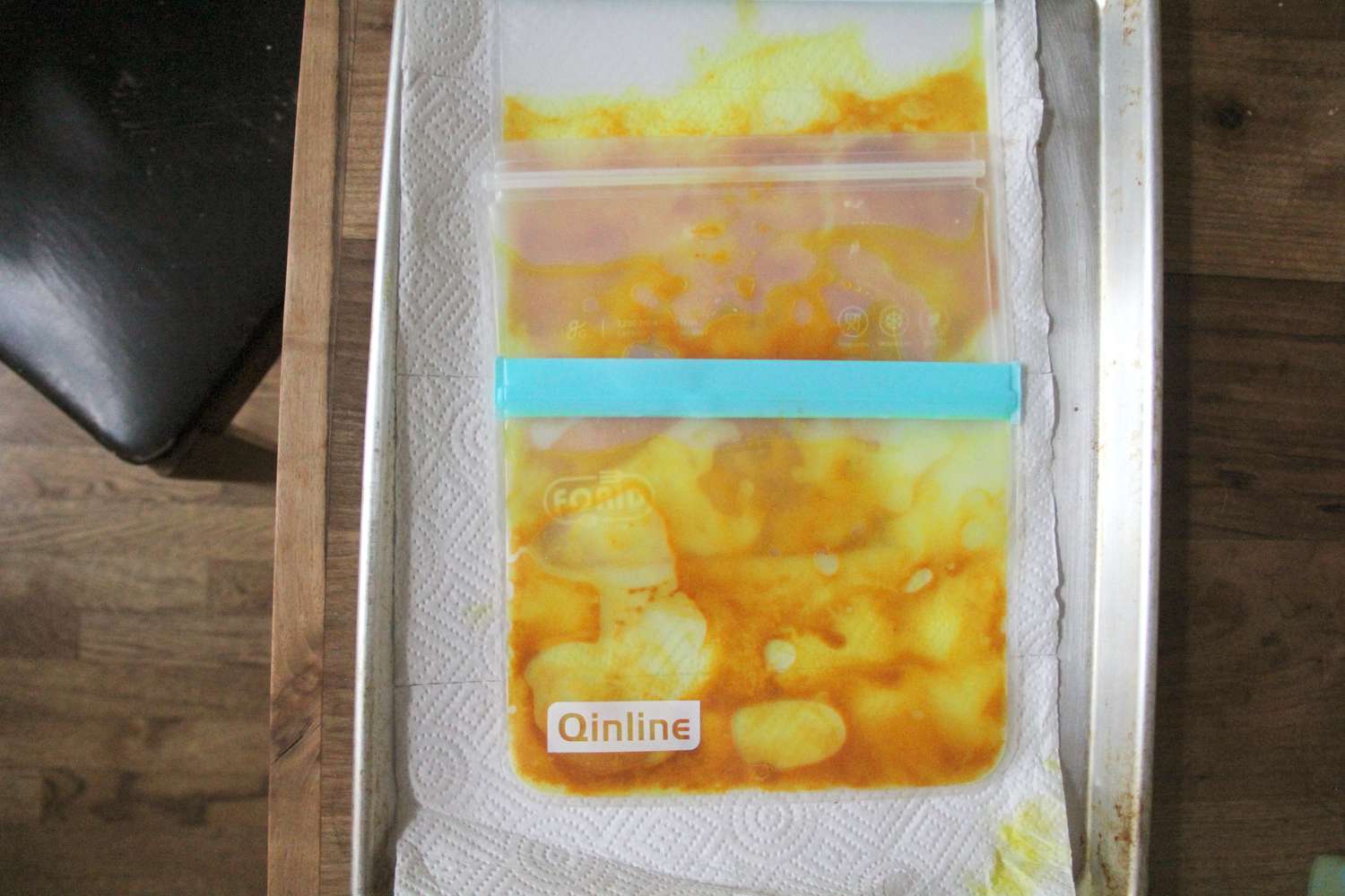Sealed bags on a tray containing food marinated with a yellow substance, laid on paper towels