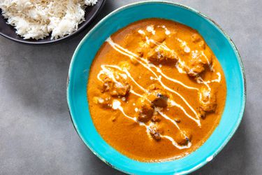 A bowl of butter chicken with a small bowl of steamed white rice next to it. 