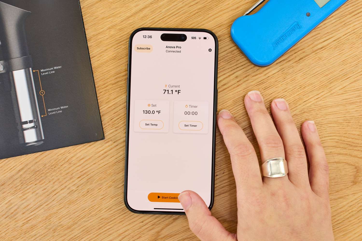 Smartphone showing the Anova Culinary Precision Cooker Pro app interface, with a hand placed nearby on a wooden table