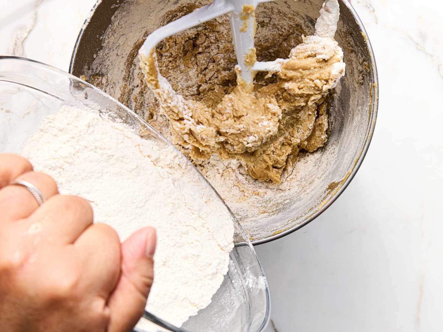 Mixing cookie dough in a stand mixer with flour being added from a bowl