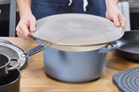 a person placing the bergkoch splatter screen over a dutch oven