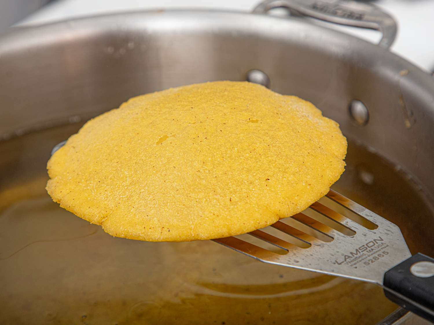 Side view of arepa being lifted out of oil