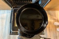 A person wears the Grill Armor Gloves BBQ Waterproof Gloves while holding a cast iron pan