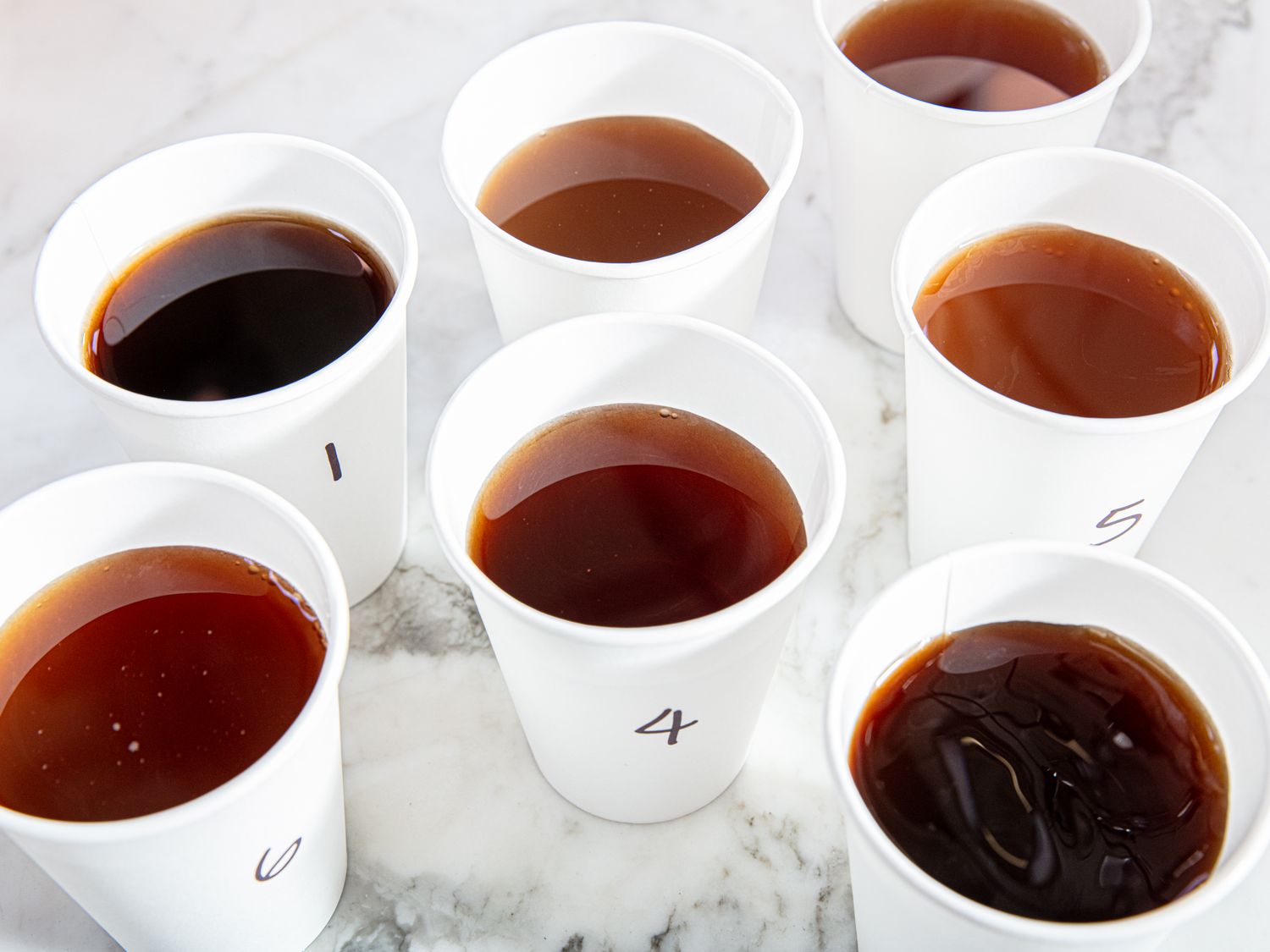 Seven numbered cups filled with iced tea on a marble surface