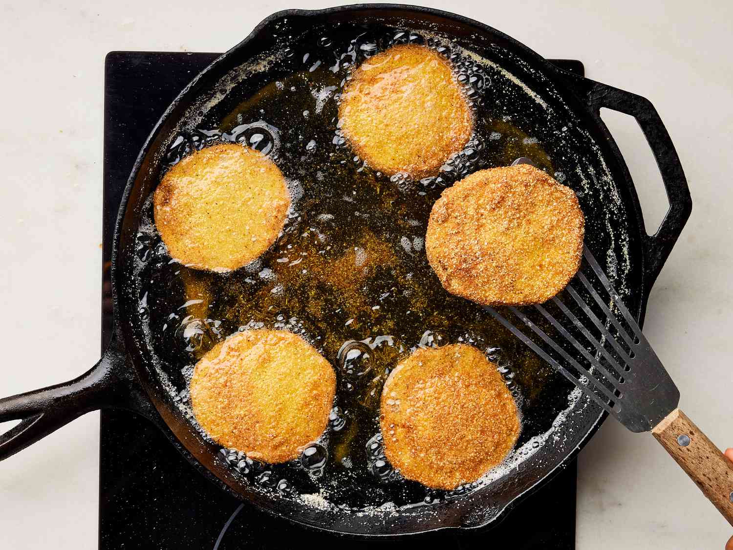 Breaded green tomatoes frying in oil in a skillet on a marble surface