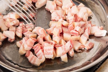 Diced pancetta in a skillet being stirred with a slotted spatula