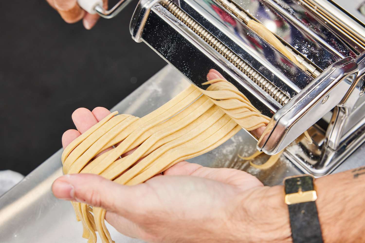 A person holding strands of fettucine as they come out of a manual pasta maker