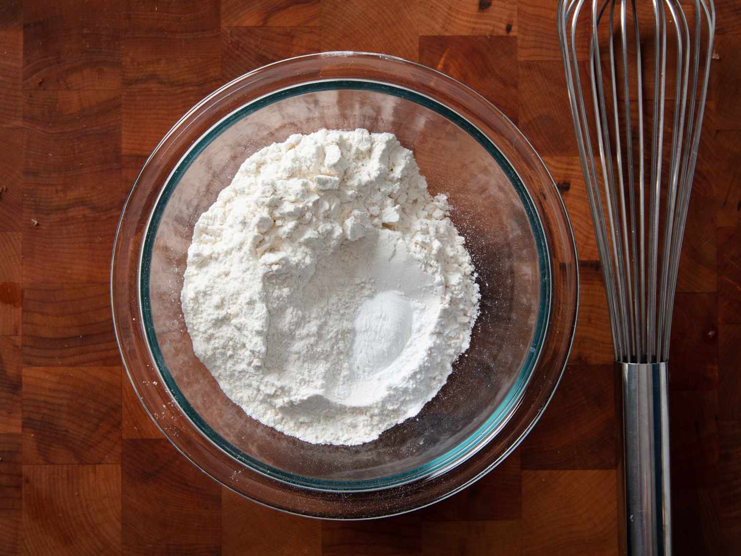Overhead shot of a whisk and bowl filled with dry ingredients for a French apple cake.